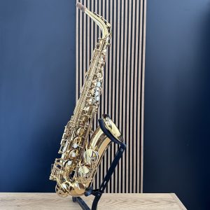 Shiny gold saxophone resting on a black stand in a music studio with a blue wall and wooden panel background.