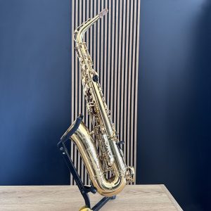 Golden saxophone on a stand in a room with a blue wall and wooden table nearby.