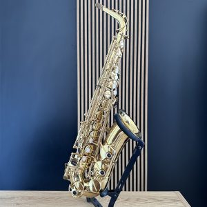 Shiny gold saxophone resting on a black stand against a blue wall and light wood floor in a studio setting.