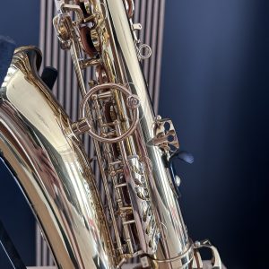 Close-up of a shiny brass saxophone showing keys, rods, and curved body against a dark background